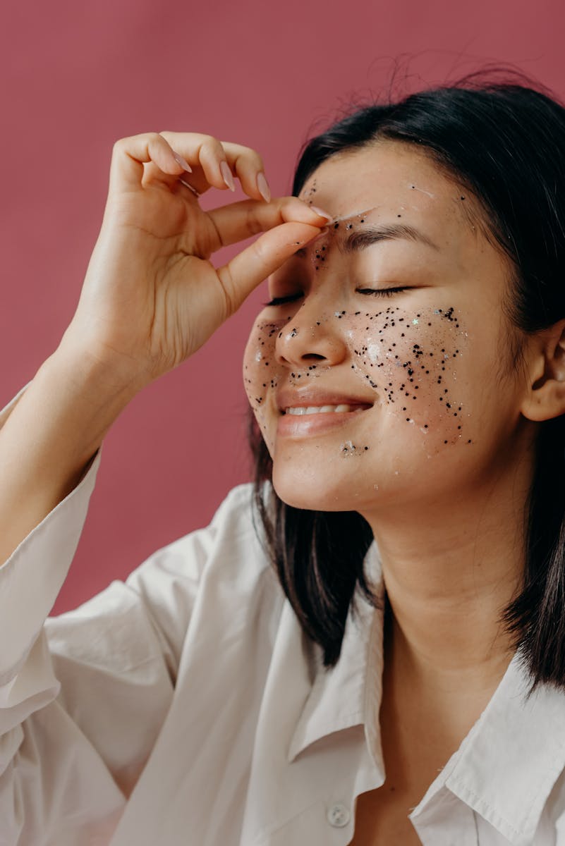 Smiling Asian woman applying a glitter face mask, enhancing her skincare routine.